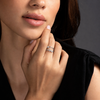 Close-up of a woman's hand with a ring on her finger, touching her face against a dark background