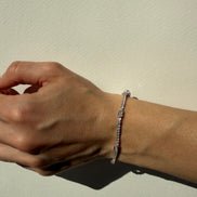 Hand wearing a silver bracelet on a neutral background