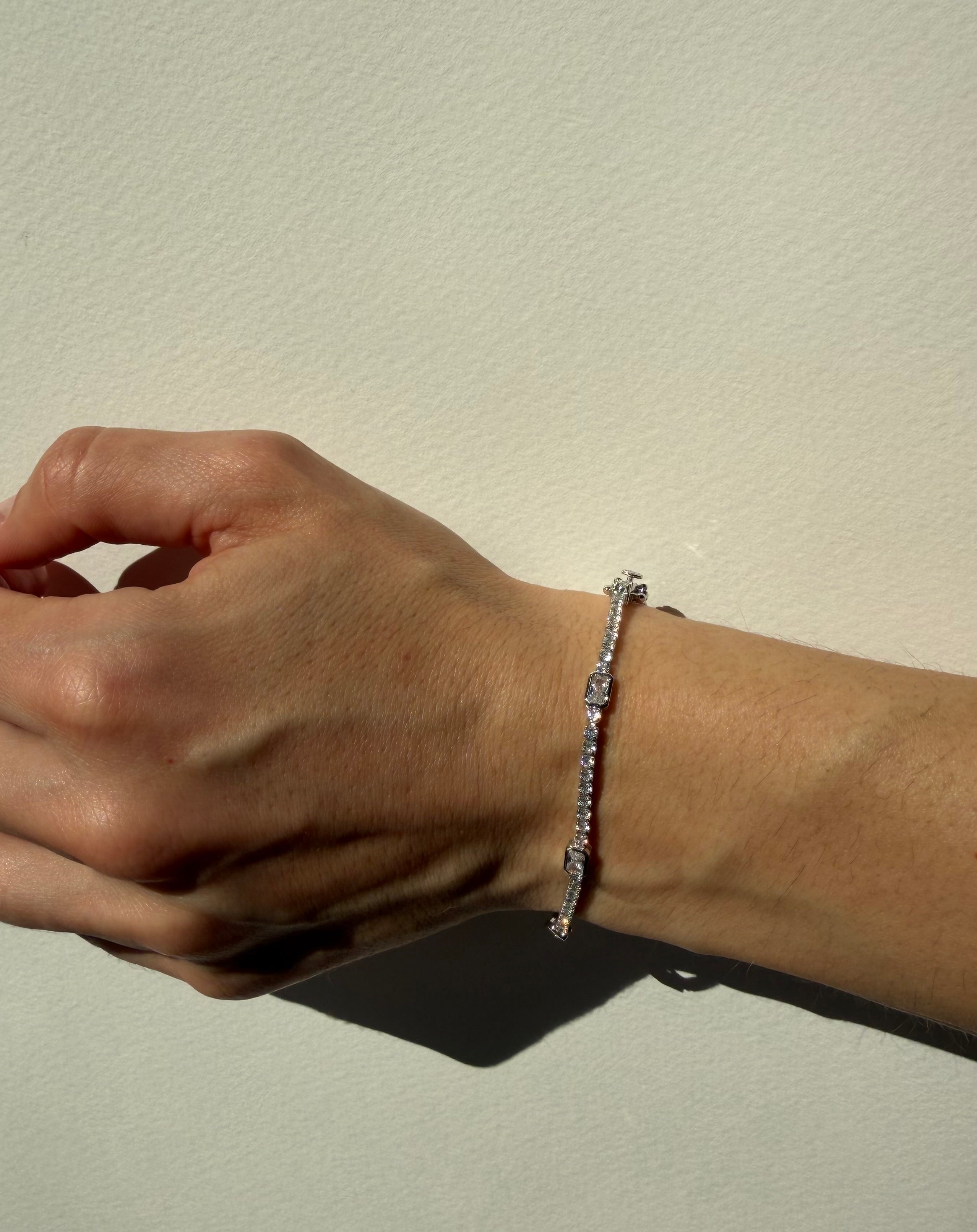 Hand wearing a silver bracelet on a neutral background