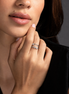 Close-up of a woman's hand with a ring on her finger, touching her face against a dark background